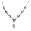 The Oval Amethyst with Pear Drop Necklace is a silver piece adorned with seven oval purple gemstones and a central teardrop-shaped gem.