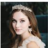 A woman with long hair wears Tiara 3, featuring floral designs with champagne and gold pearls accented by opals, along with pearl earrings and a ruffled dress, as she gazes at the camera.