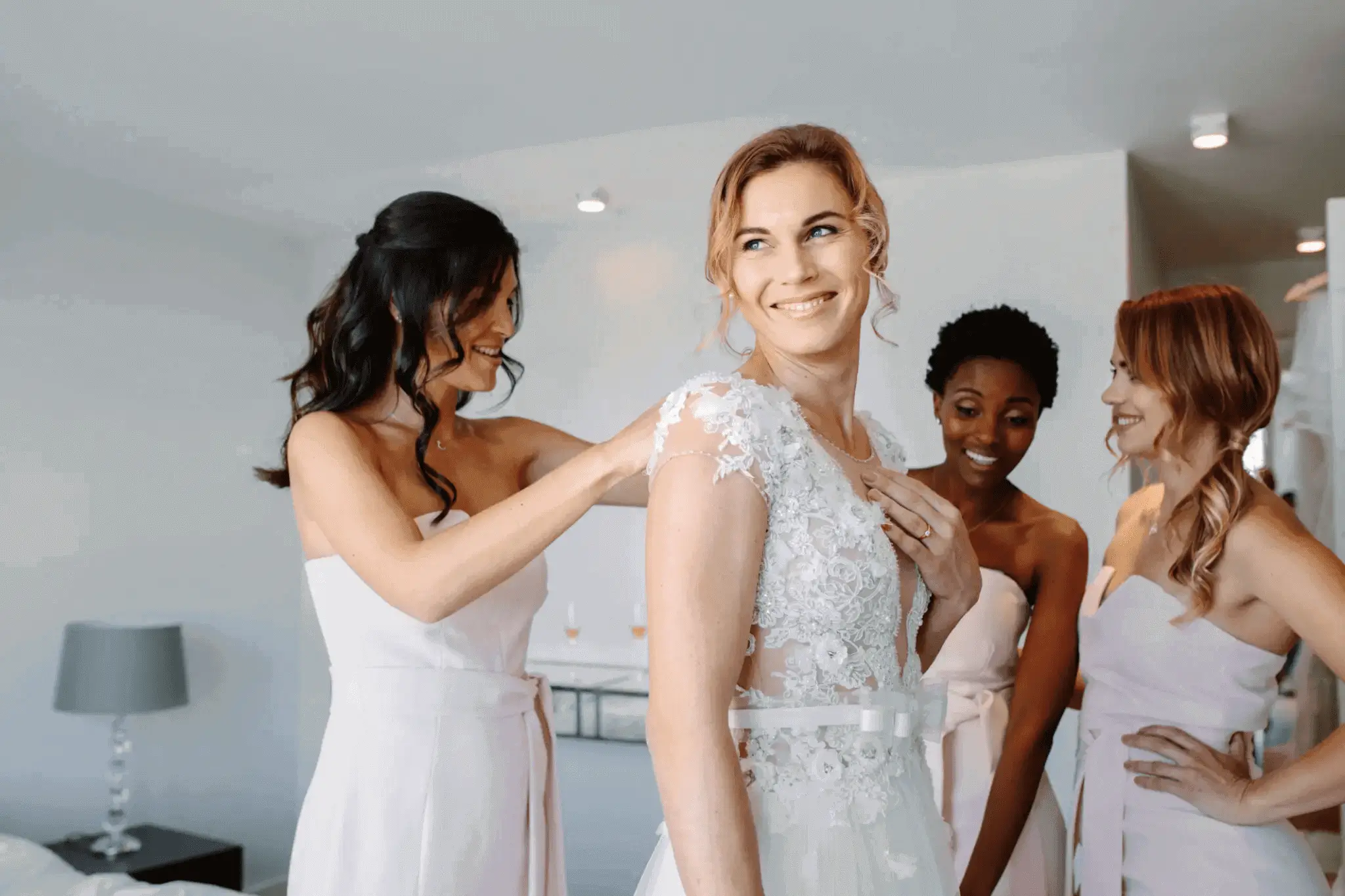 Bride surrounded by bridesmaids in blush dresses and getting ready for wedding